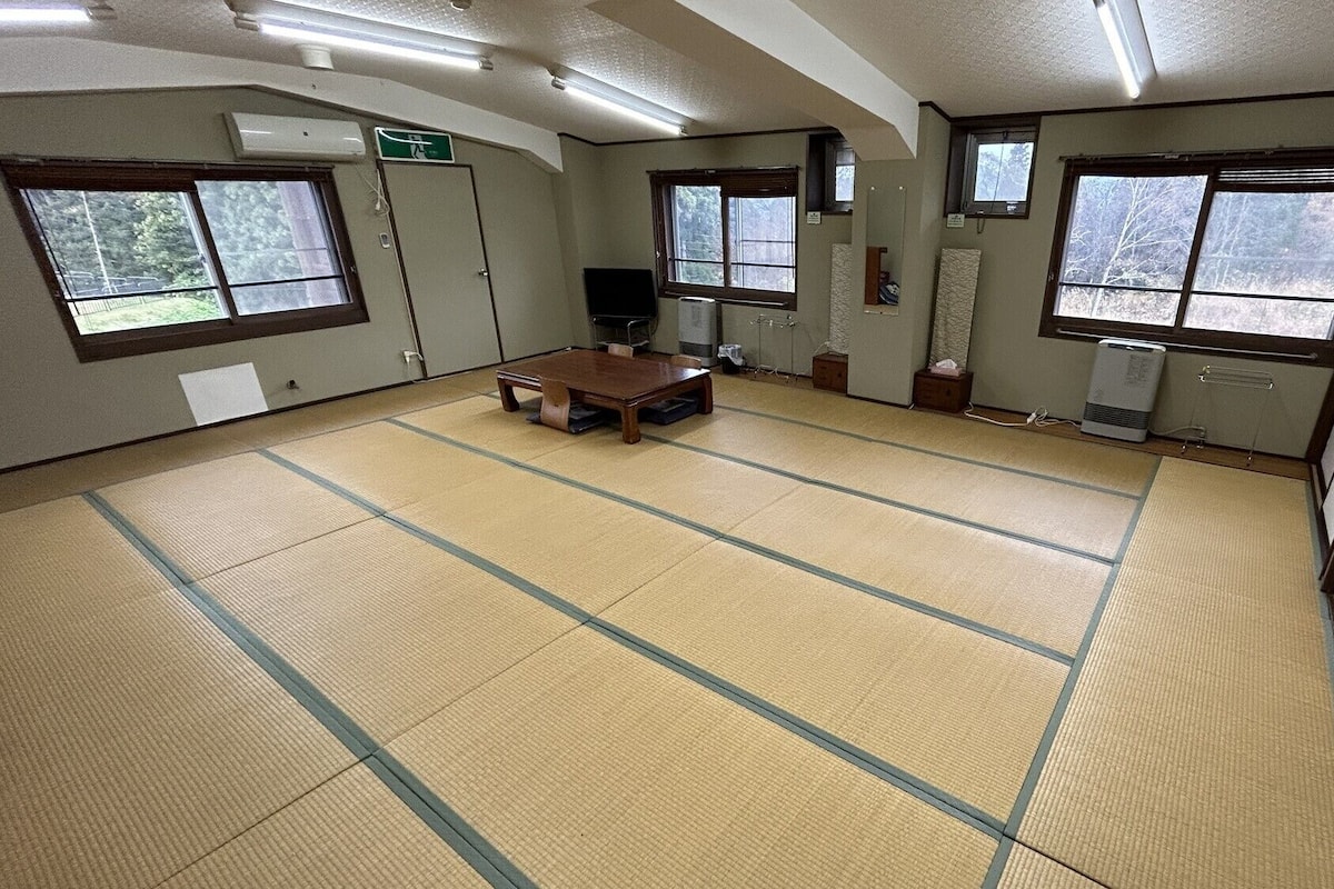 Una habitación con tatamis, una mesa de madera, ventanas y un radiador.