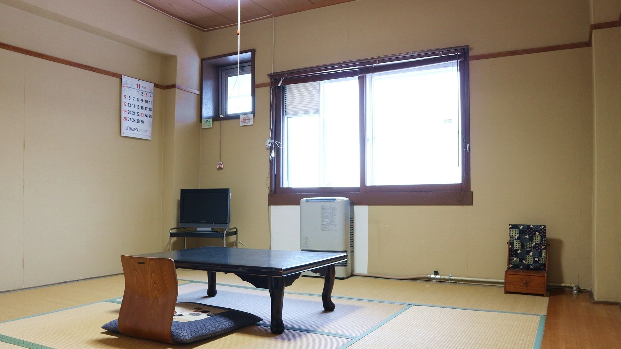 Una habitación con esteras de tatami, una mesa negra, un televisor y un ventanal grande.