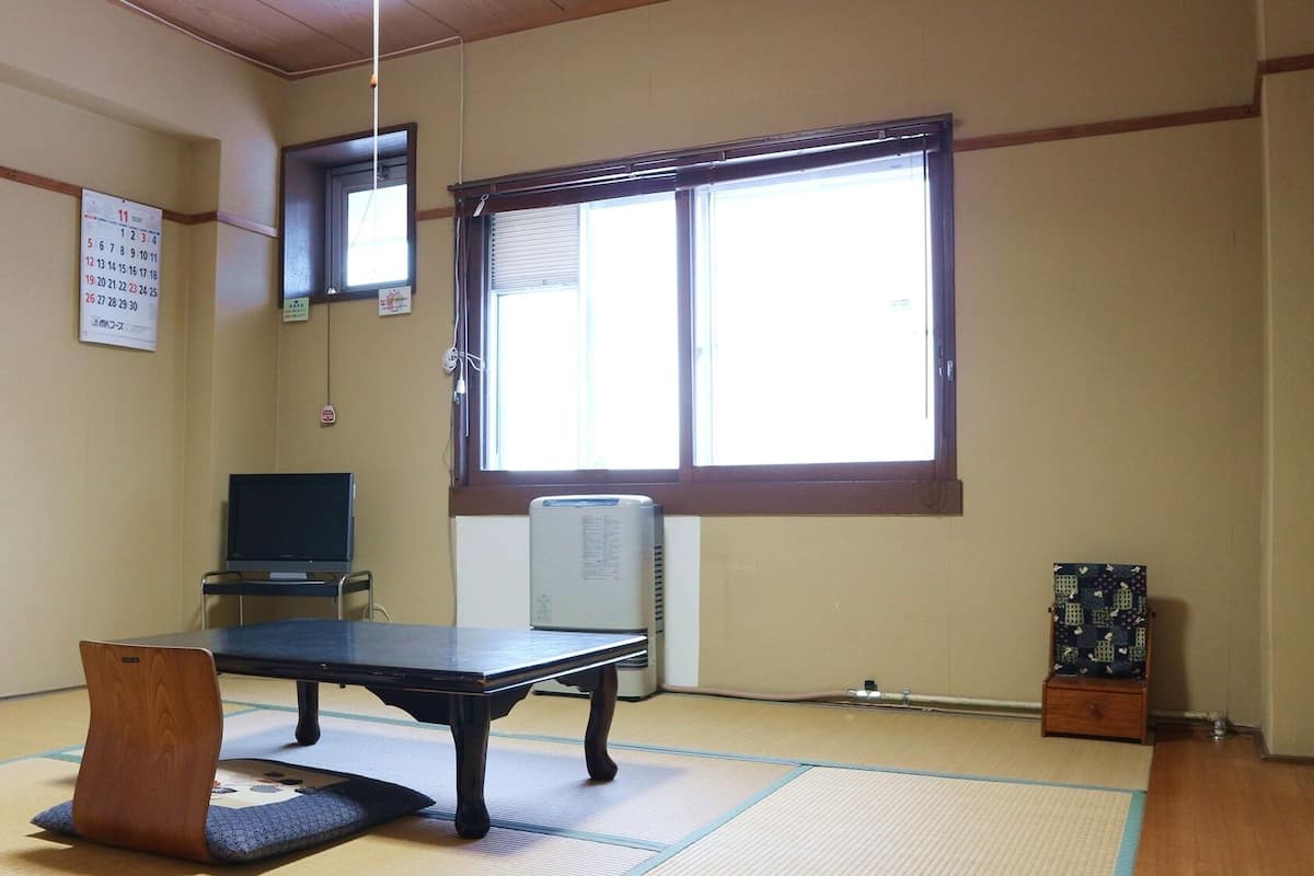 Una habitación con esteras de tatami, una mesa negra, un televisor y un ventanal grande.