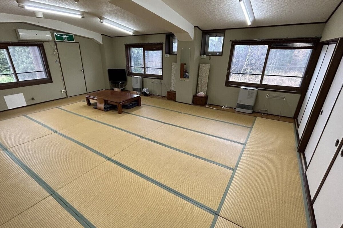 Una habitación con suelo de tatami, una mesa baja de tatami, un televisor y una colchoneta de futón.
