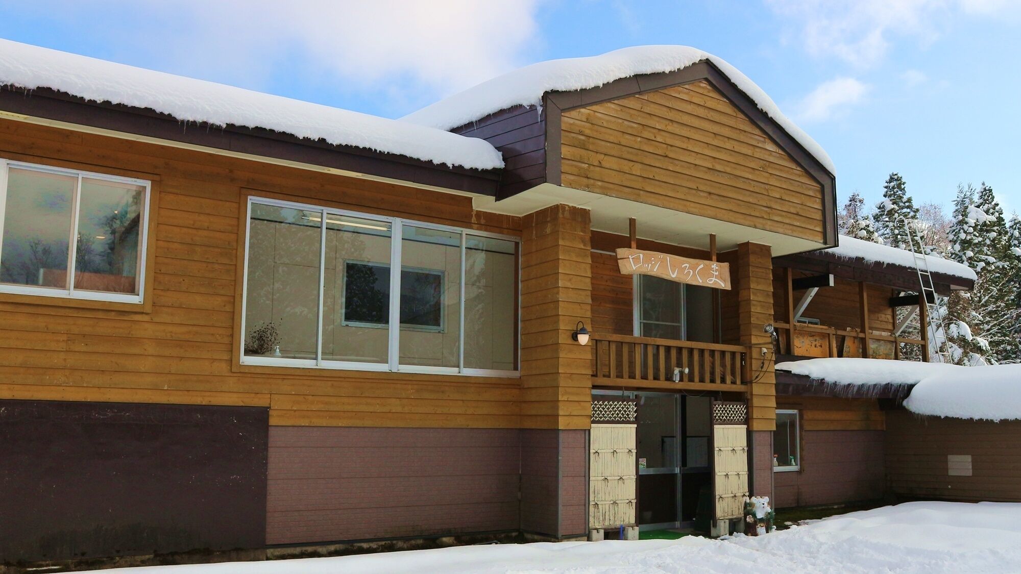 A wooden building with large windows and a balcony, surrounded by snow.