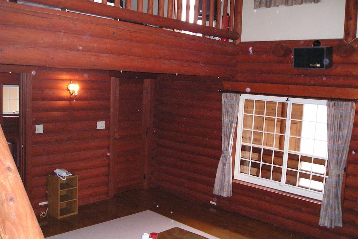 Une chambre de style rustique, avec un plafond en bois, une fenêtre avec des rideaux, une petite étagère en bois et un thermostat fixé au mur.
