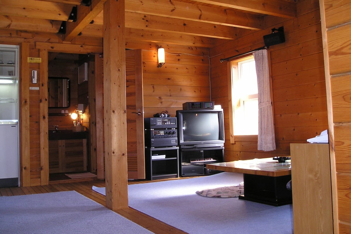 L’intérieur d’une cabane en bois comprend un coin cuisine, un téléviseur et une fenêtre.