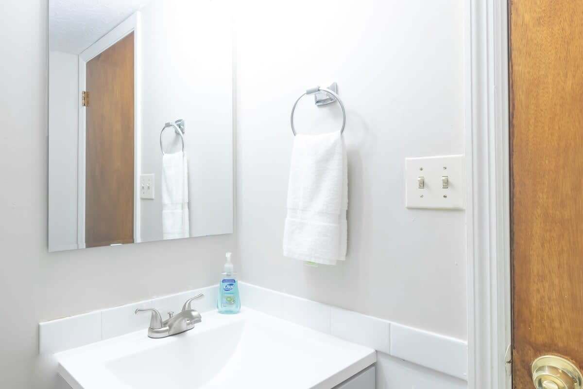 Une salle de bain avec un lavabo blanc, un miroir, un porte-serviettes et un flacon de savon pour les mains.