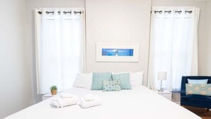 A hotel room with a large bed, two bedside tables, a chair, and a framed picture on the wall.