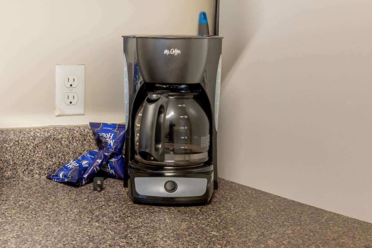 Eine Kaffeemaschine auf einer Granitabdeckung mit einer Steckdose und Kaffeekapseln in der Nähe.