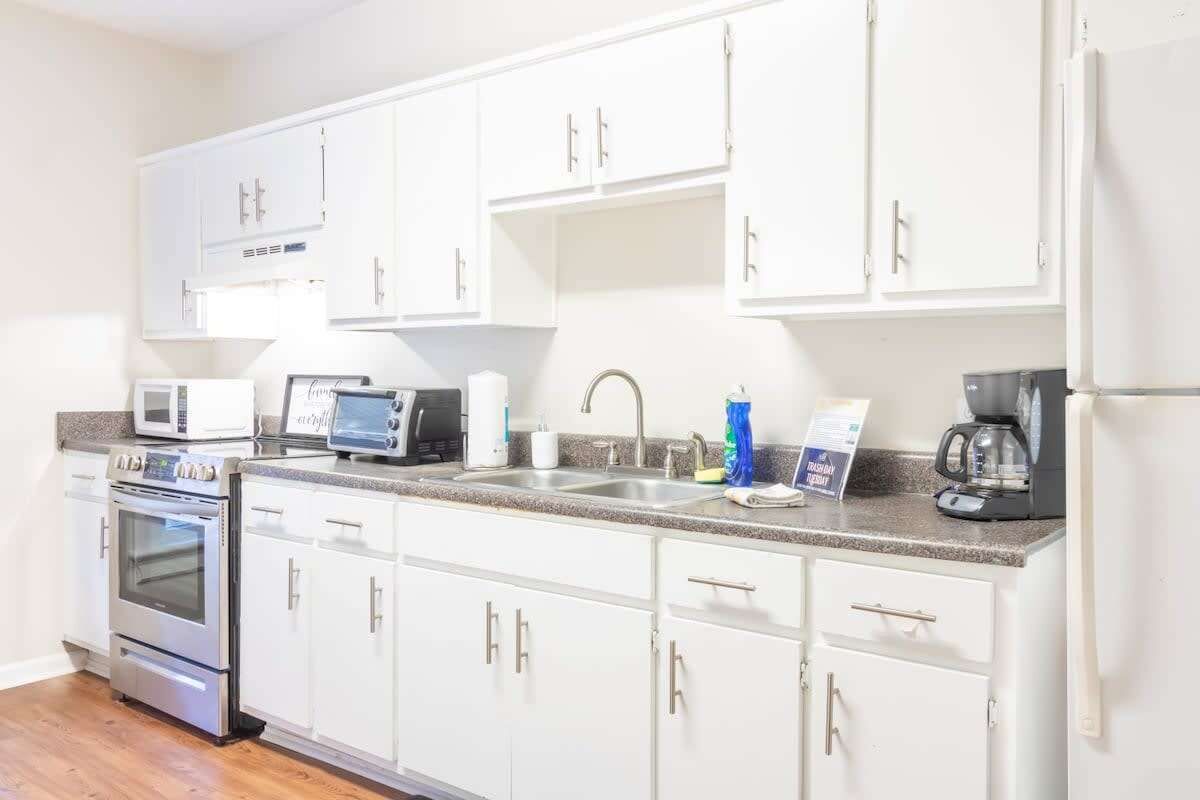 A kitchen with white cabinets, a microwave, an oven, a coffee maker, and a sink.