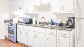 A kitchen with white cabinets, a microwave, an oven, a coffee maker, and a sink. - Historic Uptown Home w/ Porch & Parking (Columbus)