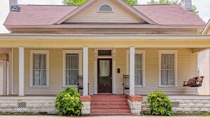 A two-story house with a front porch, a central door, and a small window above the door.