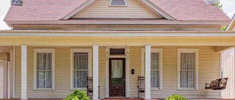 A two-story house with a front porch, a central door, and a small window above the door.