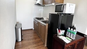 A compact kitchen with wooden cabinets, a microwave, a stove, and a refrigerator. - Golden Mile Villa (Amami)