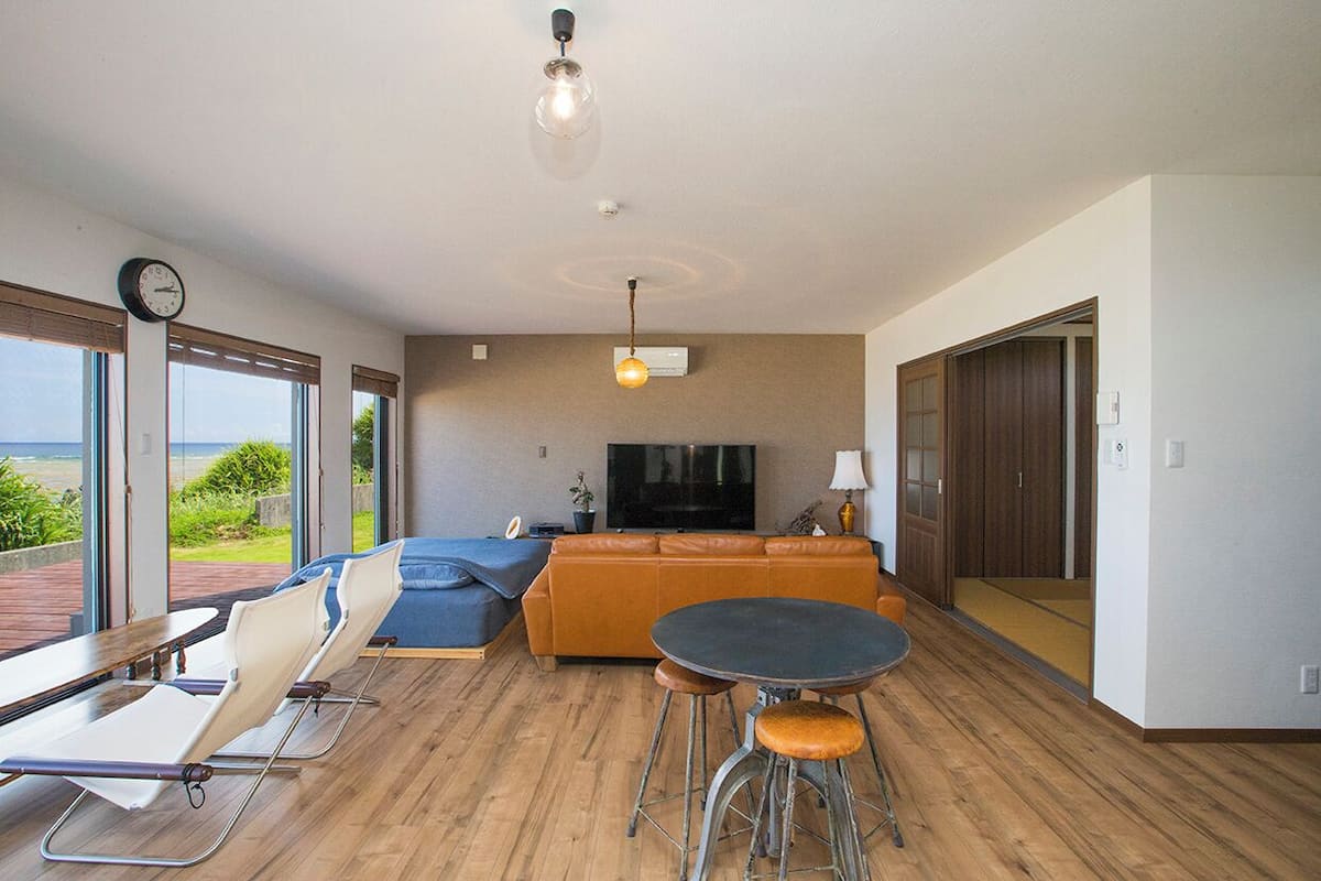 A modern living room with a sofa, a TV, a dining table, and a view of the outdoors.