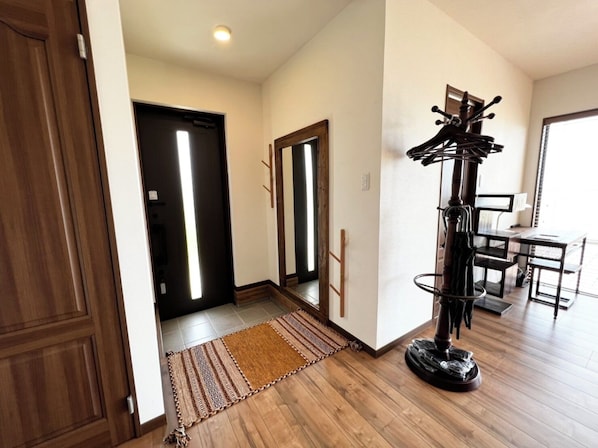 A hallway with wooden flooring, a patterned rug, a coat rack, and a door leading to another room. - Golden Mile Villa (Amami)