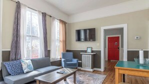 A living room with a sofa, armchair, coffee table, TV, and a red door. - Large Downtown Home - The Sunny Southern Manse (Columbus)