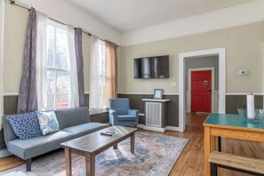 A living room with a sofa, armchair, coffee table, TV, and a red door. - Large Downtown Home - The Sunny Southern Manse (Columbus)