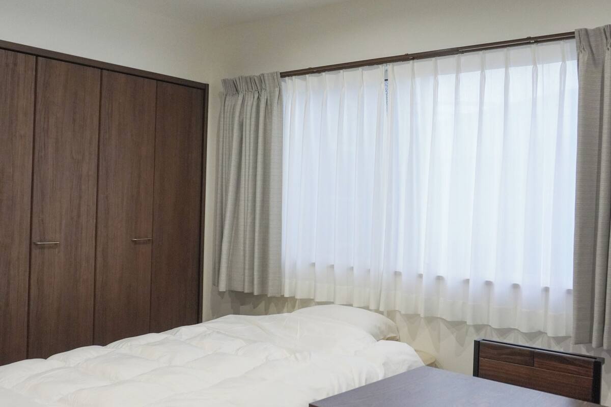 A bedroom with a bed, a wooden wardrobe, a table, and a chair.
