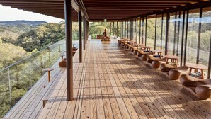 Una terraza de madera con mobiliario exterior y ventanas amplias con vista a un paisaje boscoso.