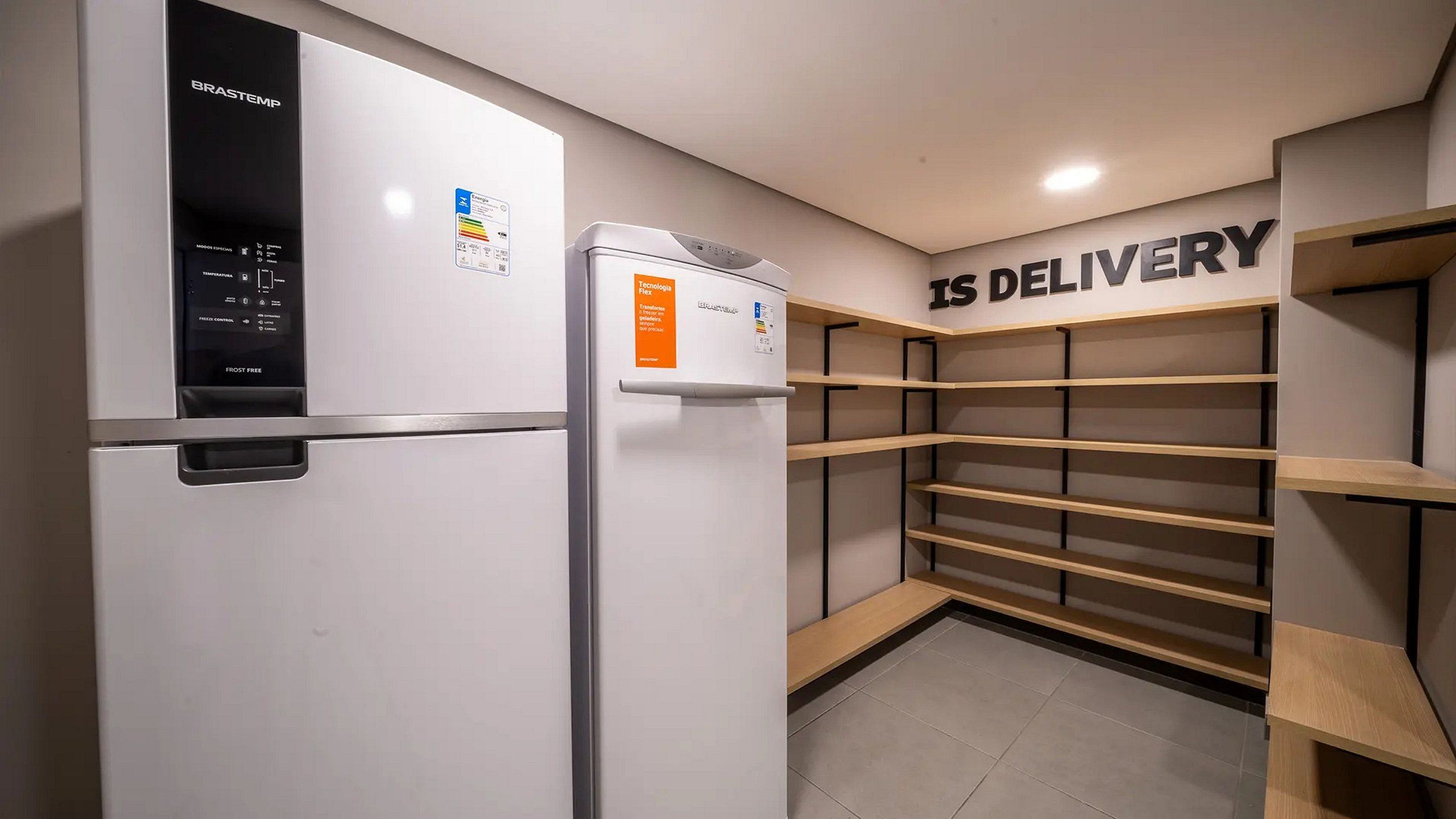A modern kitchen with two white refrigerators, a wall-mounted shelf unit, and a sign that reads 'IS DELIVERY'.
