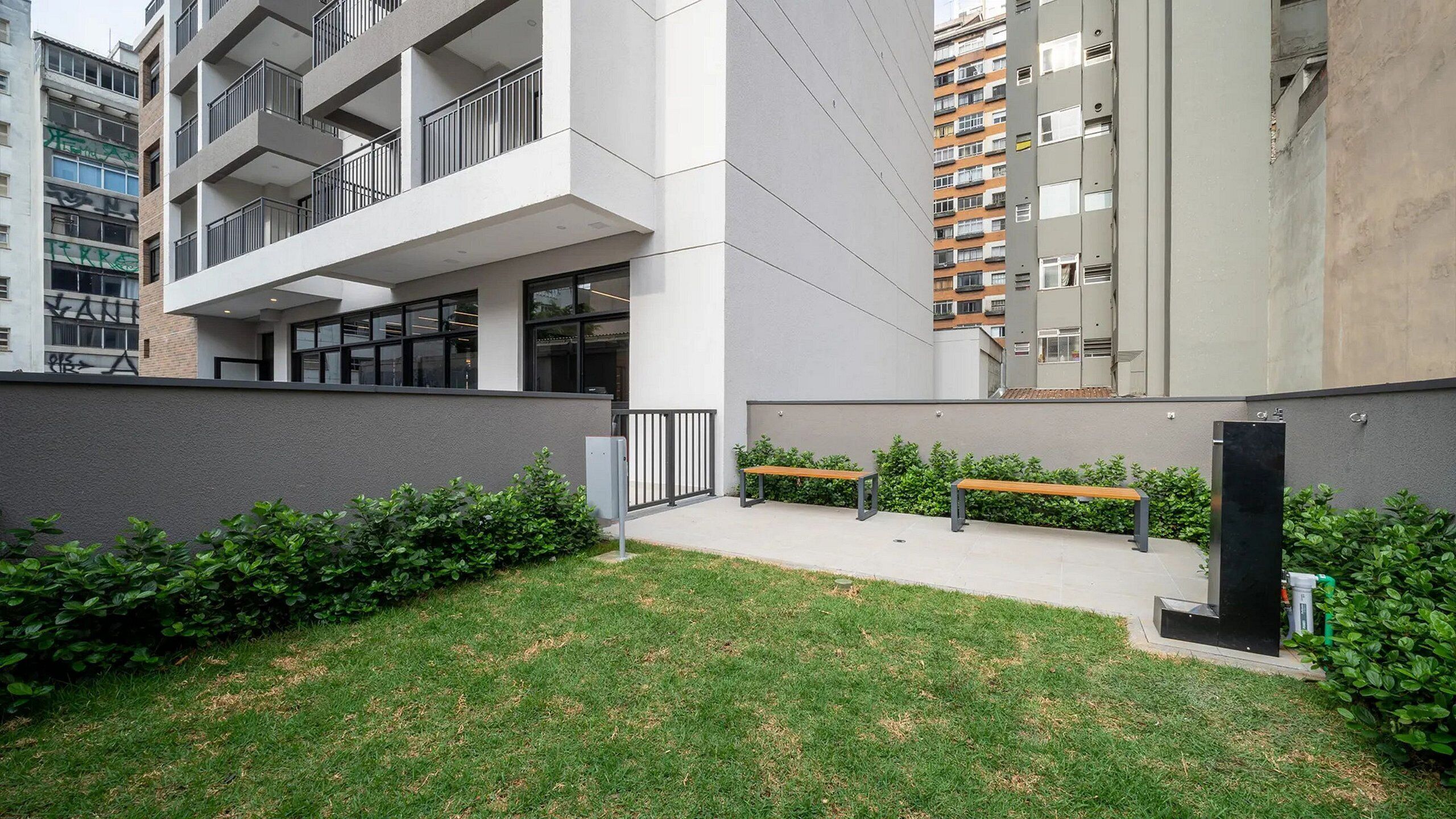 A modern building with a flat roof, large windows, and a small courtyard with benches and greenery.
