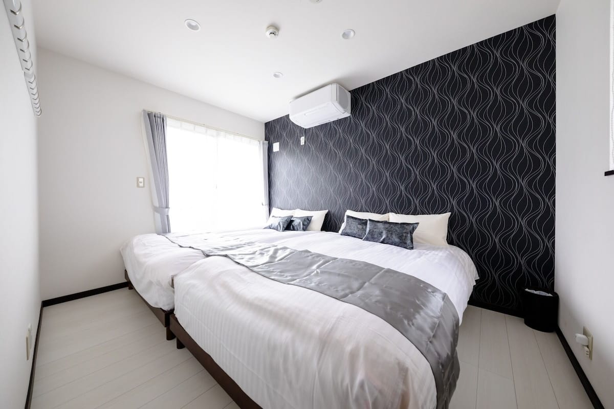 Une chambre à coucher avec un lit, une fenêtre avec des rideaux, un climatiseur fixé au mur et un mur décoré d’un motif.