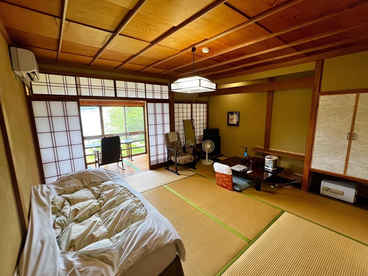 Een traditionele Japanse kamer met tatami vloeren, een bed, een bureau, een stoel en een ventilator.