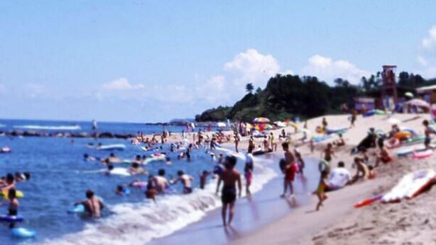 A crowded beach with people swimming and walking along the shore. - Suikeisyoku No Shiteiseki Koya (Yurihama)