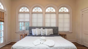 A bedroom with a large bed, a grey headboard, and three arched windows with blinds. - Midtown Main House w/ BBQ, Pets OK, Near Downtown (Columbus)
