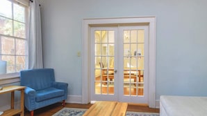 A room with a blue armchair, a wooden table, a patterned rug, and a sliding glass door leading to a dining area. - Midtown Main House w/ BBQ, Pets OK, Near Downtown (Columbus)