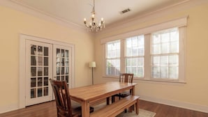 A dining room with a wooden table and chairs, a chandelier, large windows with blinds, and a door with glass panels. - Midtown Main House w/ BBQ, Pets OK, Near Downtown (Columbus)
