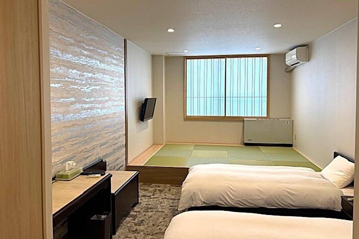 A hotel room with a bed, a desk, a television, and a large window.