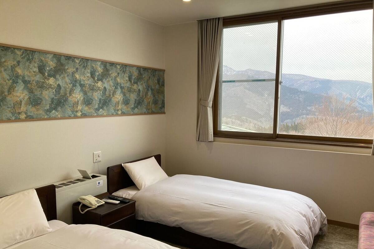 A hotel room with two beds, a painting on the wall, a window with a mountain view, and a telephone on the nightstand.