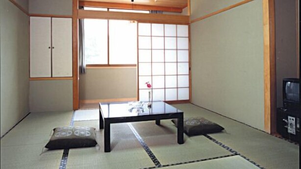 Een traditionele Japanse kamer met tatami vloerbedekking, een lage tafel, kussens, schuifdeuren en een televisie.