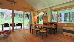 A wooden interior with a dining area, chairs, a table, and a large window with a forest view. - Morinonakano Kissatooyado Morikurasu (Maniwa)
