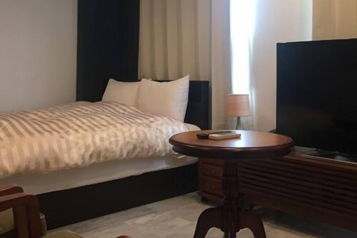 A hotel room with a bed, a television, a small table, and a window with curtains.