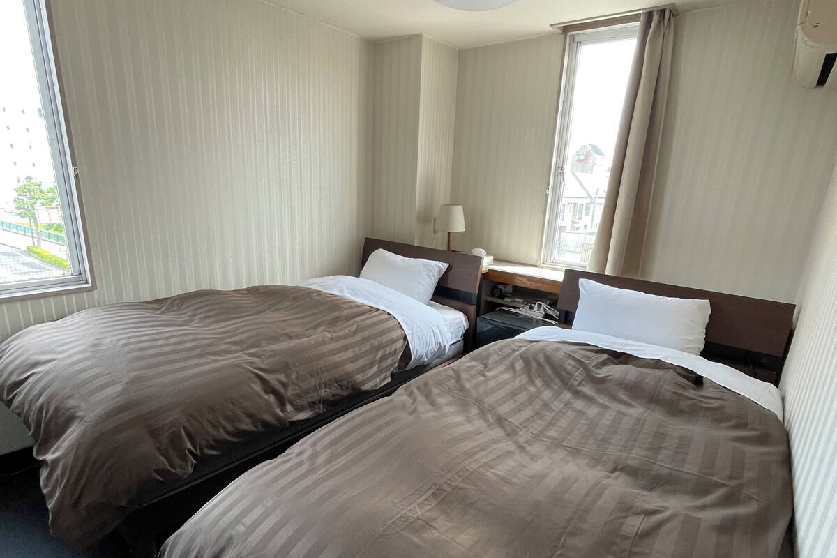 A hotel room with two beds, a window, a lamp, and a ceiling light.