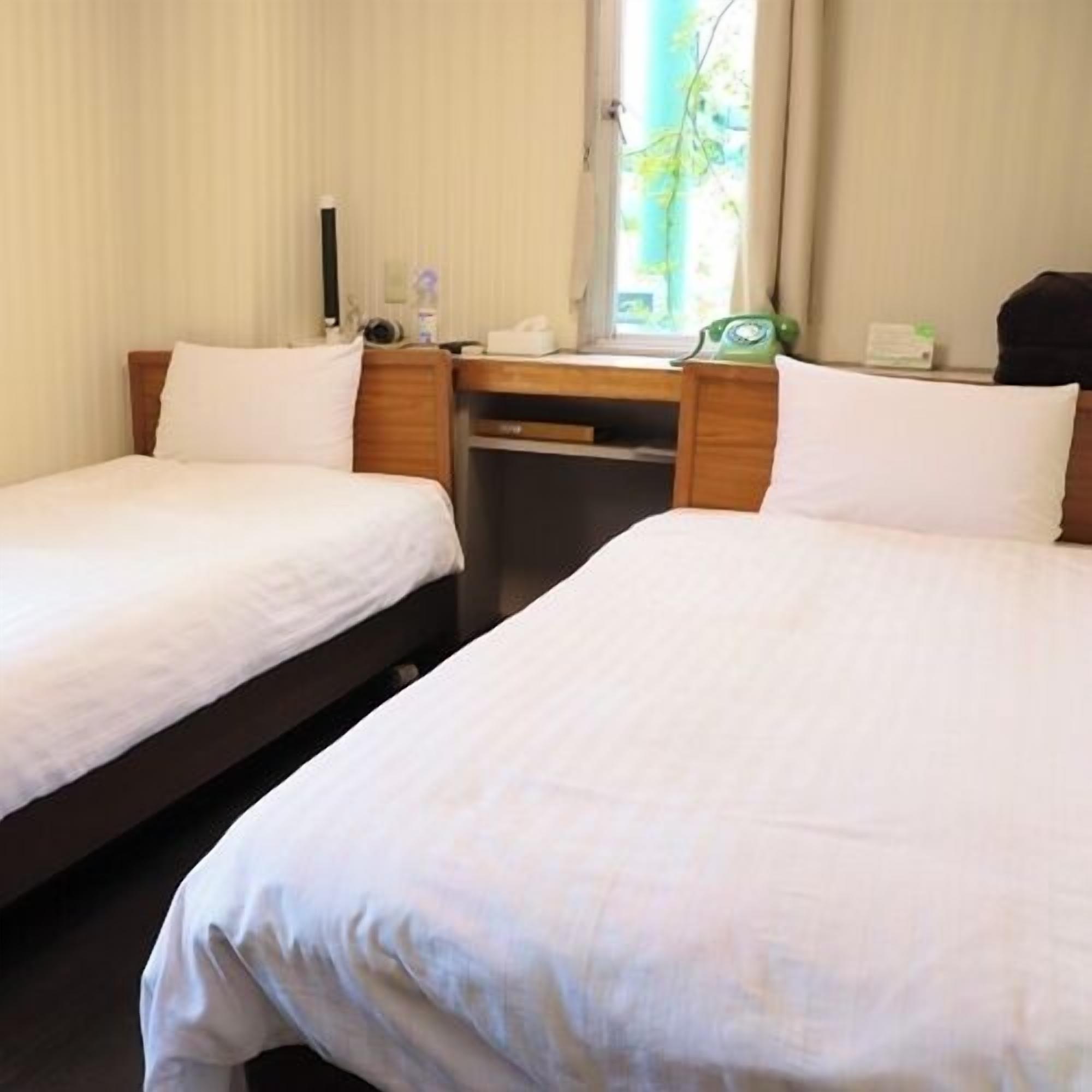 Quarto de hotel com duas camas, uma mesa, um telefone e uma janela com cortinas.