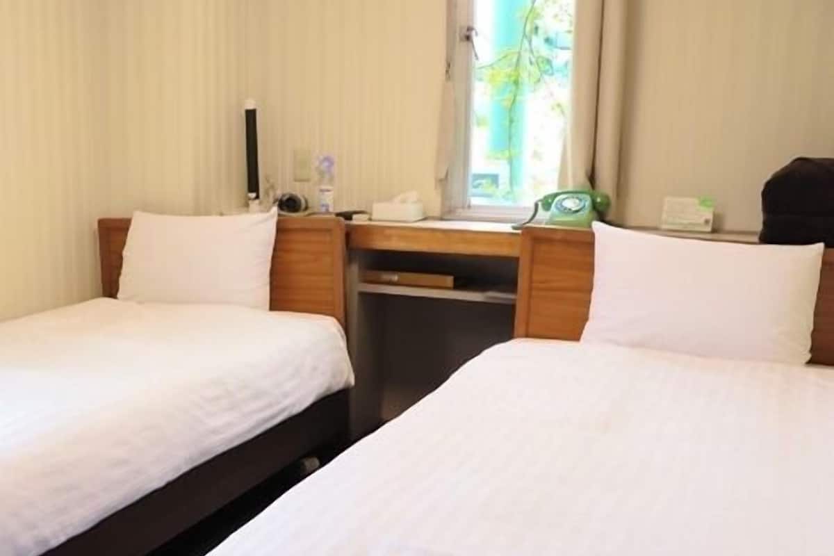 A hotel room with two beds, a desk, a telephone, and a window with curtains.