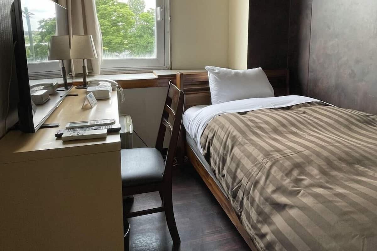 A hotel room with a bed, desk, chair, lamp, and a window with curtains.