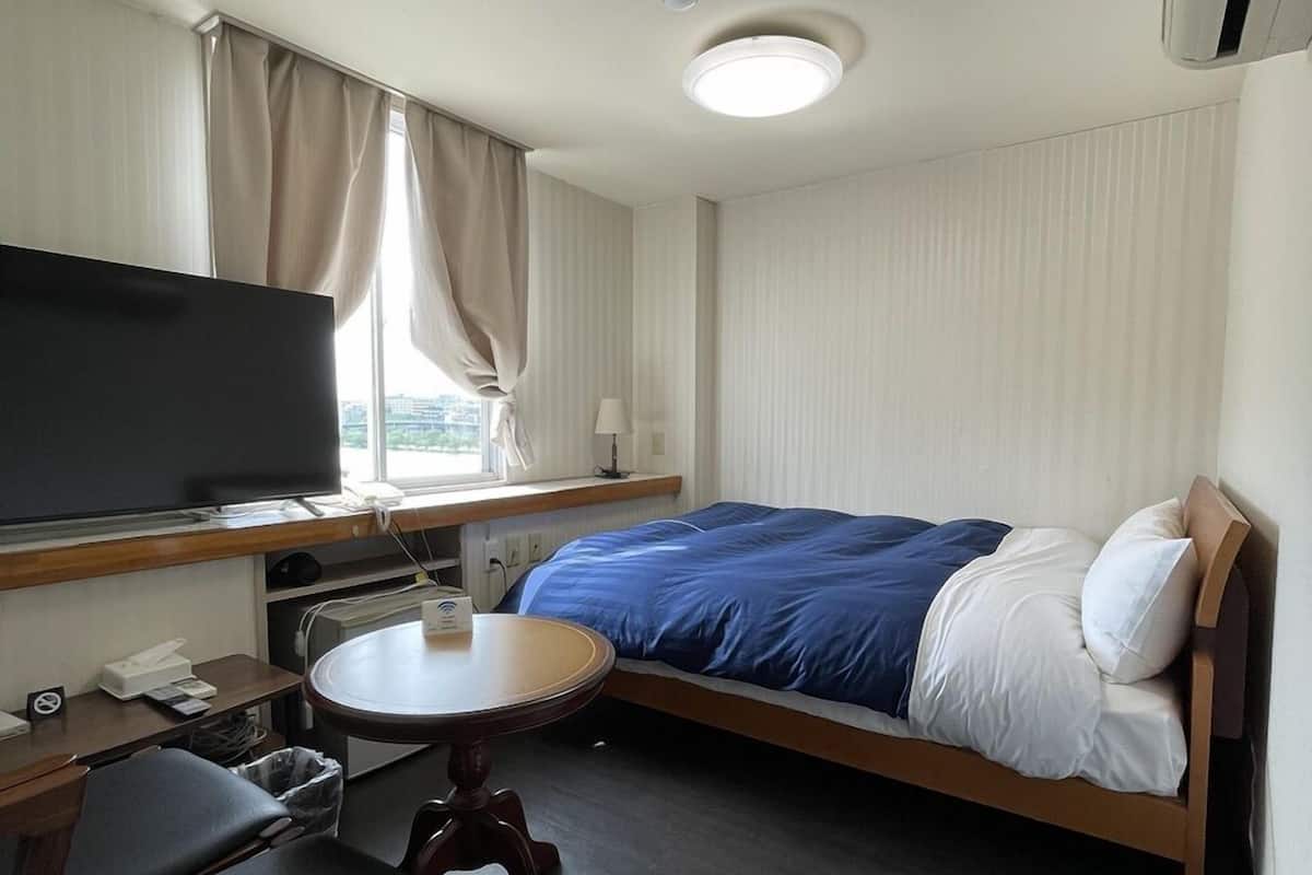 A compact hotel room with a bed, a desk, a chair, a television, and a window with curtains.