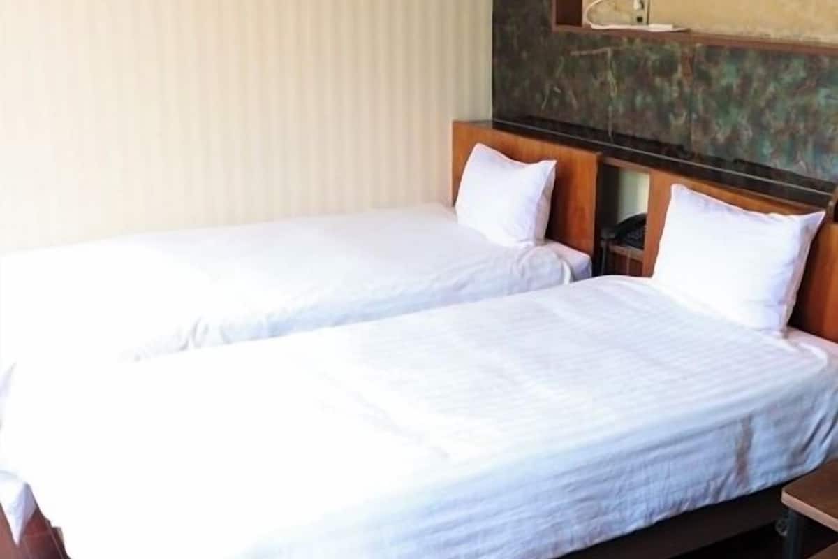 A hotel room with two single beds, wooden headboards, a nightstand, and a wall-mounted shelf.