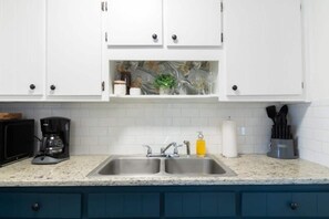 A kitchen with white cabinets, a double sink, a coffee maker, and a knife block. - Centrally Located- The Delightful Doubles Unit E (Columbus)