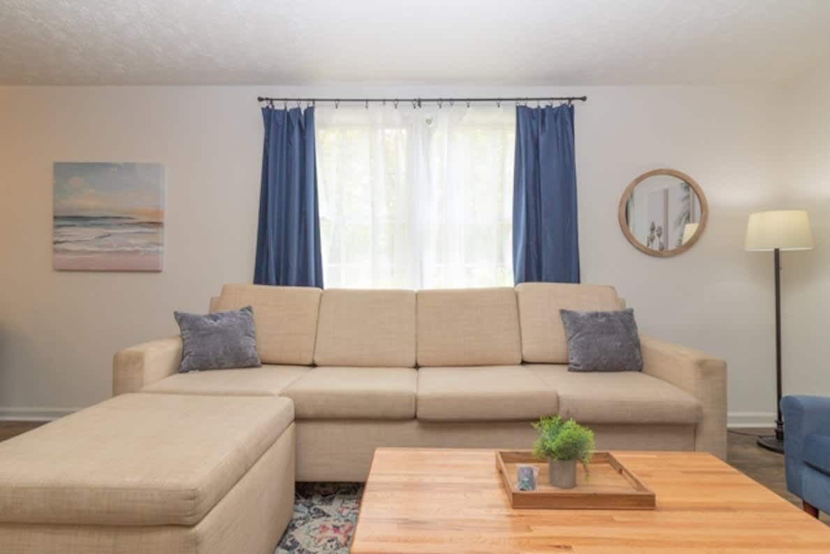 A living room with a sofa, ottoman, and a coffee table with a plant.