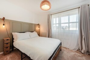 Ein Schlafzimmer mit Bett, Nachttischlampen, einem Fenster mit Vorhängen und einer Hängelampe.