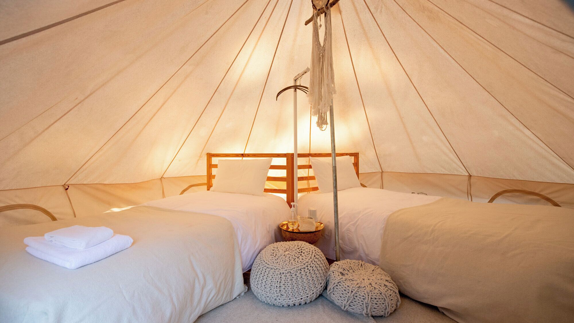 A tent with two beds, a hanging light, and a small table with a bowl.