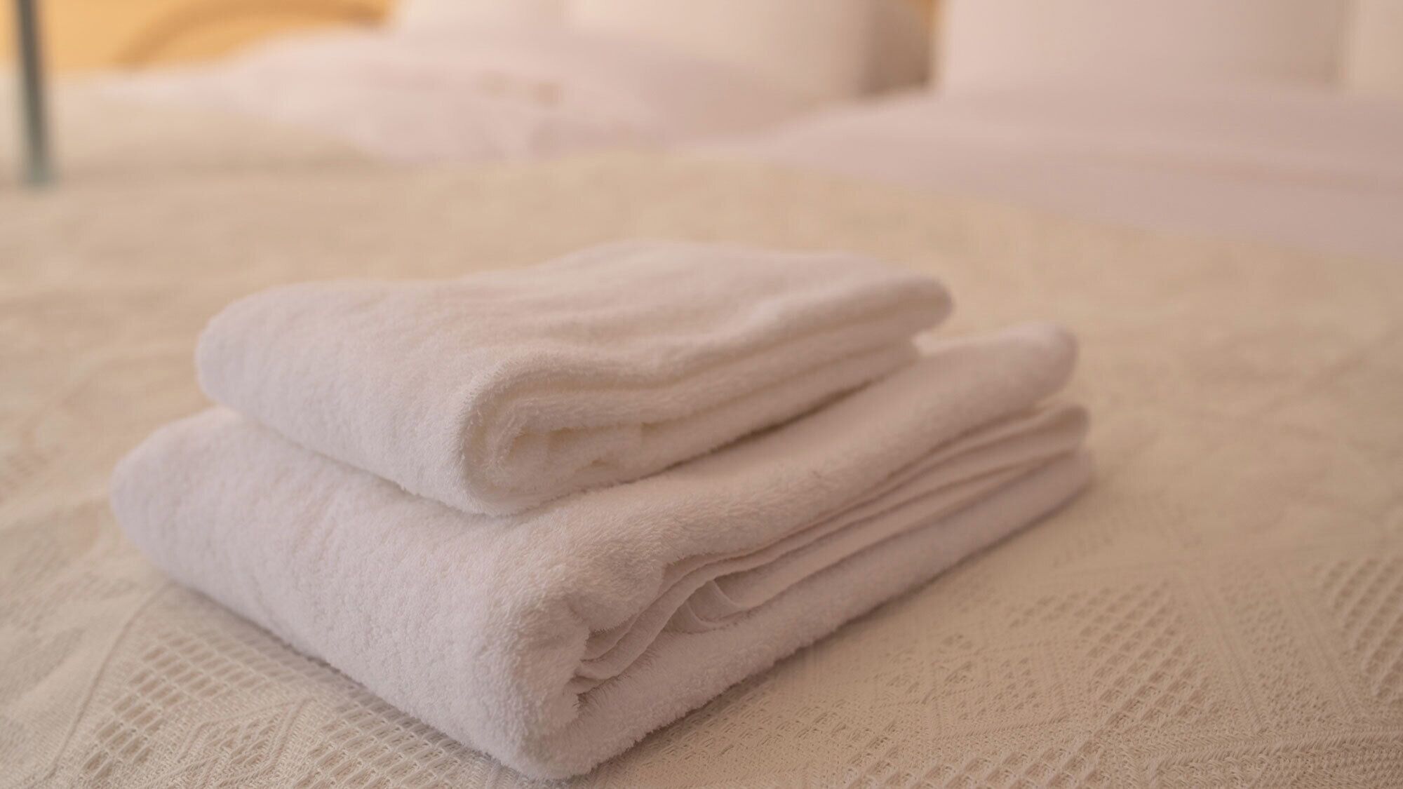A stack of folded towels on a textured white bedspread.