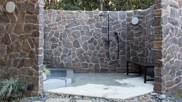 A stone-walled outdoor shower area with a bench, a hose, and a circular light fixture. - Small Planet Camp & Grill (Chiba)