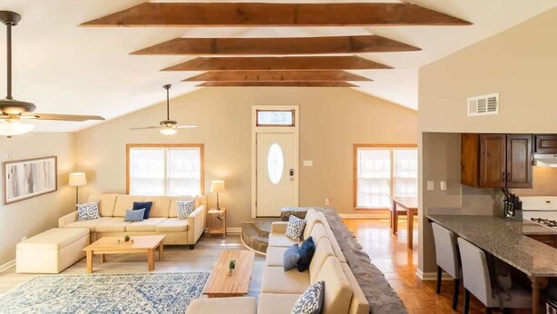 A spacious living area with a high ceiling, wooden beams, a sofa set, a coffee table, and a kitchen area with a countertop and chairs. - Pet-Friendly Condo w/ Free Parking, Near Downtown (Columbus)