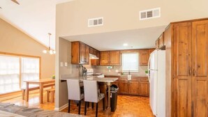 A kitchen with wooden cabinets, a dining area with chairs, a stone fireplace, and a window with blinds. - Pet-Friendly Condo w/ Free Parking, Near Downtown (Columbus)