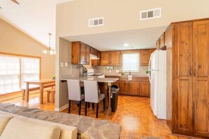 A kitchen with wooden cabinets, a dining area with chairs, a stone fireplace, and a window with blinds. - Interior Stonework, Great Spot- Delightful Doubles (Columbus)