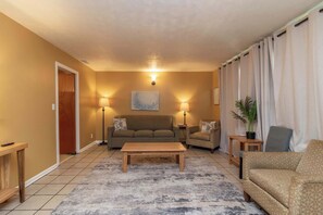 Ein Wohnzimmer mit einer Couch, einem Couchtisch, einer Lampe, einem Sessel und einer Zimmerpflanze.